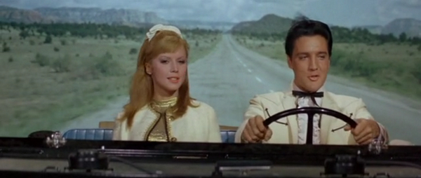 Elvis and friend behind the wheel of a large automobile