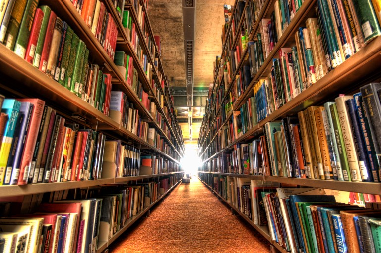 Photograph of a long corridor of bookshelve apparently stretching off endlessly into a white light at the vanishing point