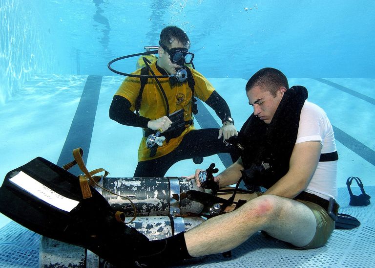 US_Navy_050209-N-3093M-004_Naval_Diving_and_Salvage_Training_Center_instructor_stands_ready_to_offer_assistance_to_a_diver_student_if_he_is_not_able_to_regain_his_own_air_supply_during_a_problem_solving_exercise_at_the_pool_con